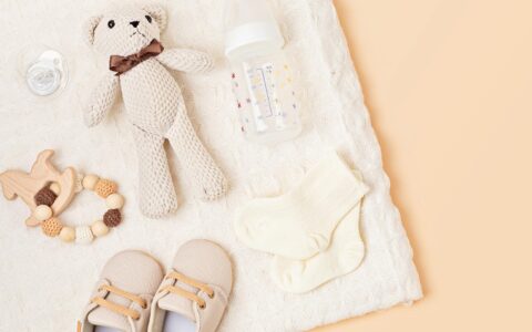 Teddy bear, baby bottle, and baby shoes spread out on a blanket