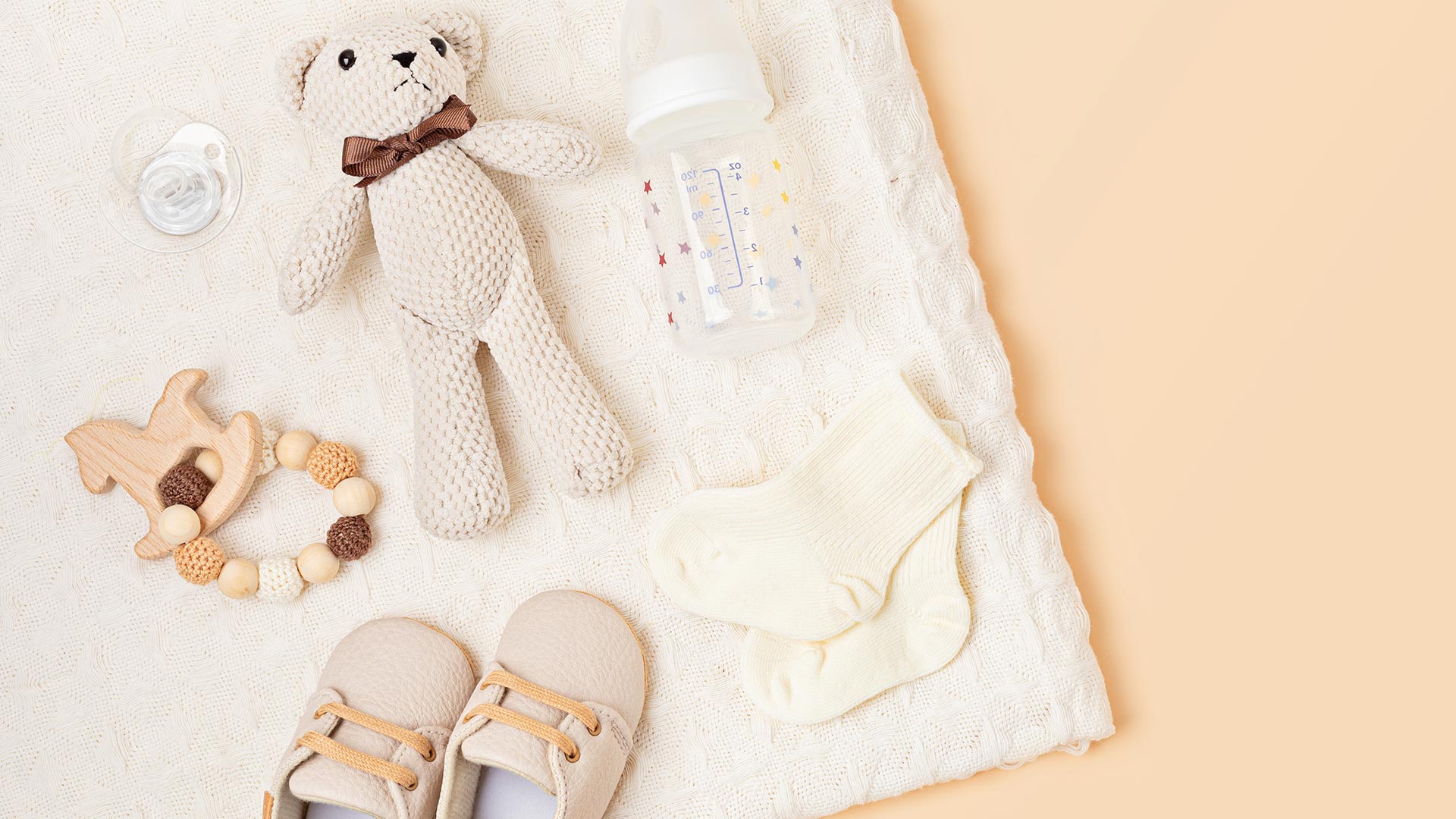 Teddy bear, baby bottle, and baby shoes spread out on a blanket