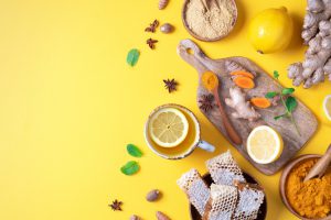 Ginger, turmeric, lemon, honey, and a variety of spices are strewn across a table, in bowls and on cutting boards.