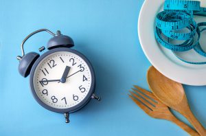 An alarm clock sits next to a plate with a blue measuring tape piled on top.