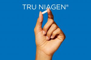 A hand holds a Tru Niagen capsule.