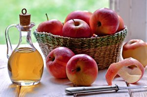 apples in a basket and vinegar in a bottle on a white table