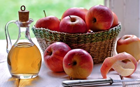apples in a basket and vinegar in a bottle on a white table