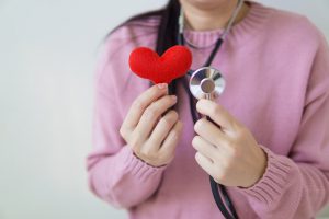 Woman holding a red felt fabric heart and a stethoscope.