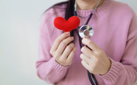 Woman holding a red felt fabric heart and a stethoscope.