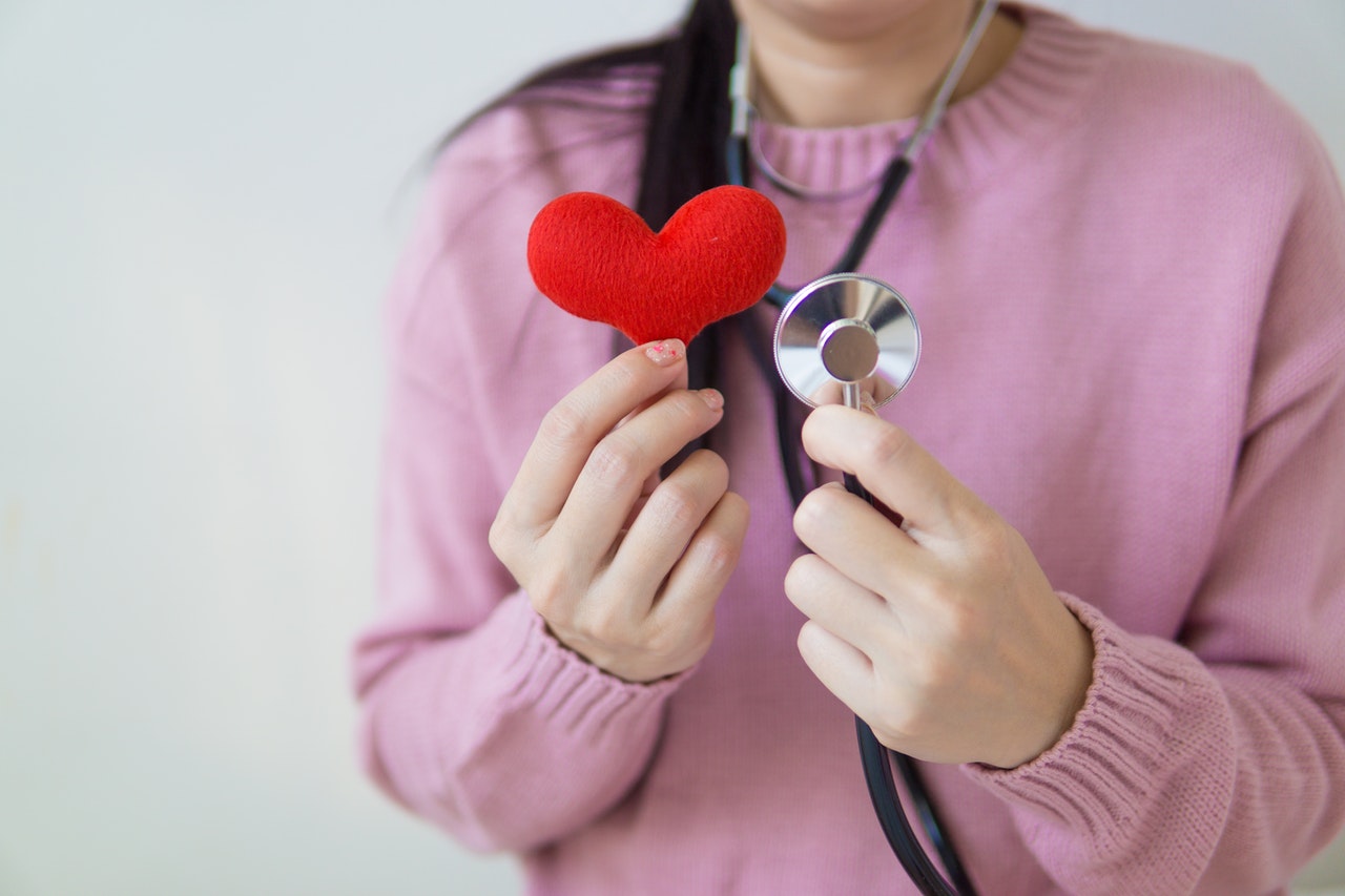 Woman holding a red felt fabric heart and a stethoscope.
