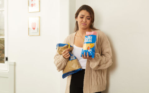 Woman appearing distressed holding 2 bags of chips.