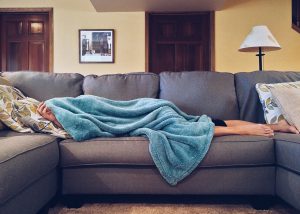 persona laying on couch with a blanket over