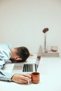 Guy sitting at table with his head down and his hand on a cup of coffee.