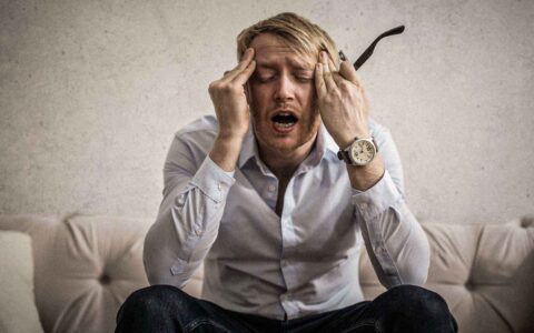 man appearing stressed holding his eye glasses