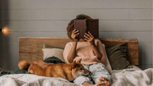 woman reading a book in bed with her dog