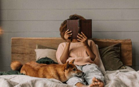 woman reading a book in bed with her dog