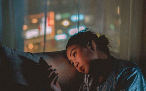 woman scrolling through her phone appearing tired