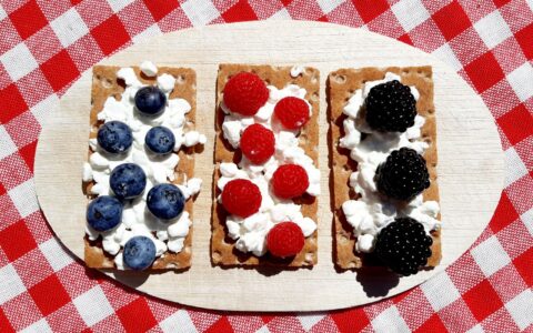 Festive snack board with crackers topped with fresh strawberries, blueberries, and cream cheese for a red white and blue Fourth of July inspired healthy appetizer